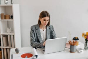 Mulher no escritório em seu notebook pesquisando sobre Certidão negativa de débitos tributários para prestar contas de sua empresa perante a receita federal.