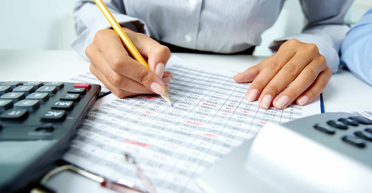 Mulher com um lápis e uma calculadora fazendo cálculos enquanto estuda sobre o código tributário municipal de seu município em um artigo da Sticorp